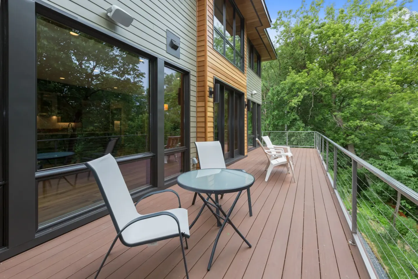 Outdoor deck with wire railing and chairs and table with trees on the background