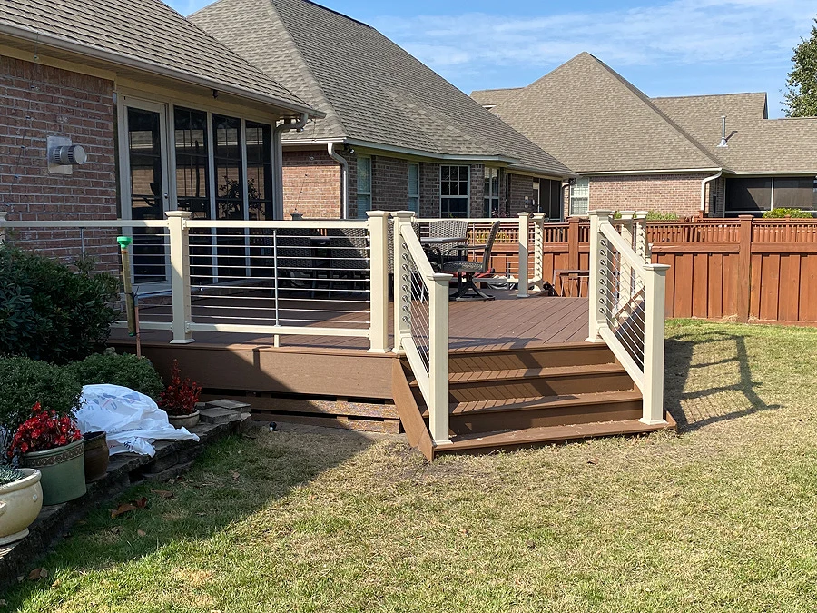 Residential wood deck installation with white vinyl wire railing and a wooden fence with outdoor furniture
